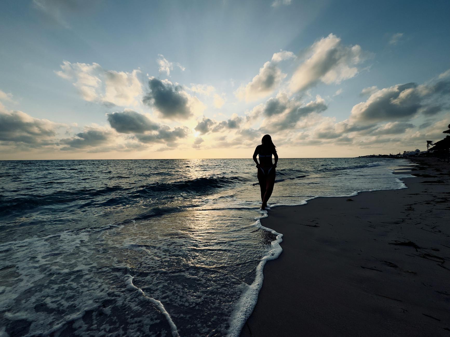 Kobieta w sylwetce idzie o zachodzie słońca po plaży w Tunezji