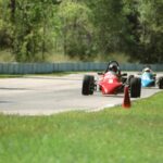 Dwa bolidy wyścigowe pędzące po torze w otoczeniu drzew