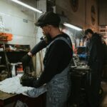 Najlepsze zamienniki części do Peugeotów: co warto kupować, a czego unikać Dwóch mechaników naprawia samochód w przyciemnionym warsztacie Peugeot