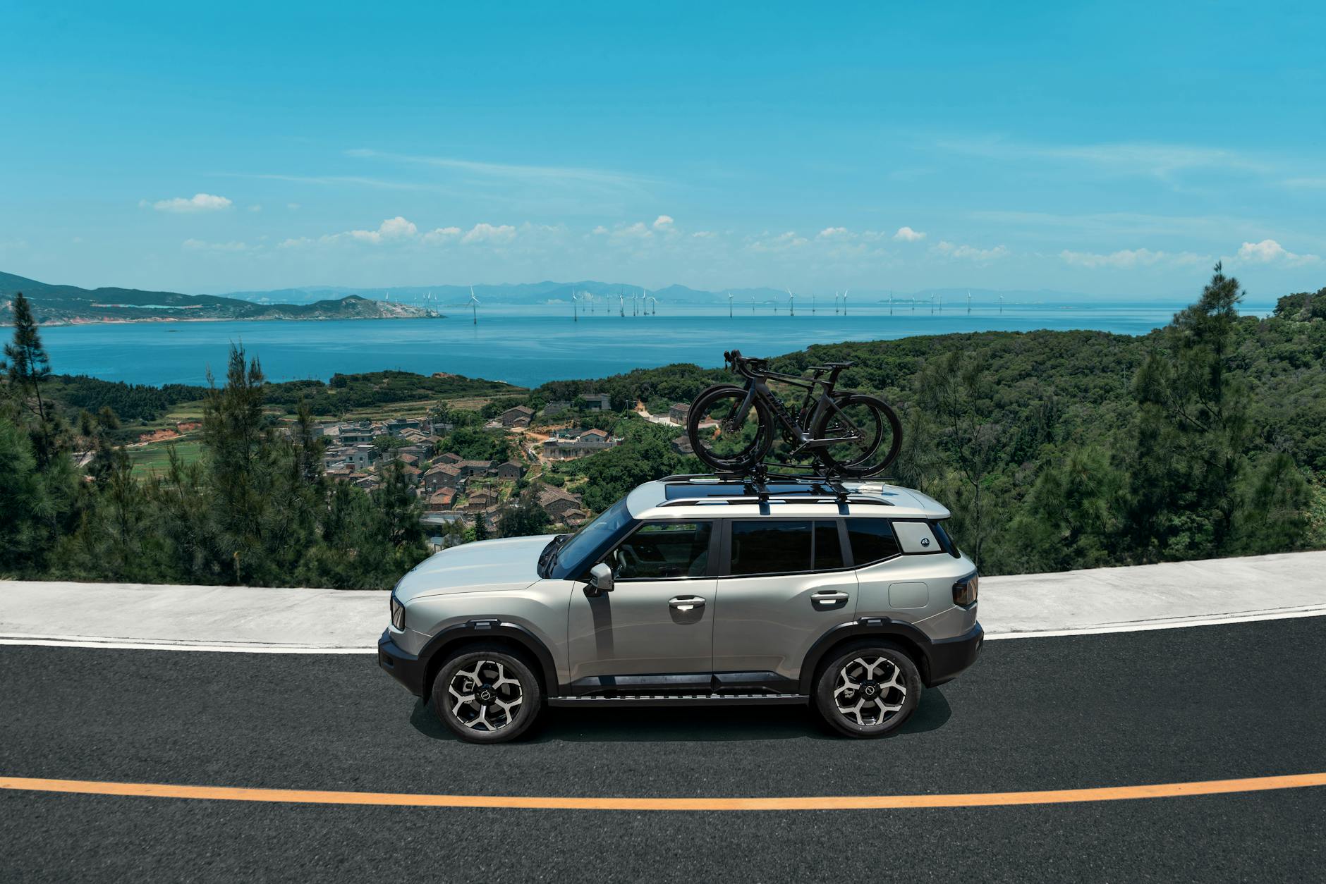 Srebrny SUV z rowerami na dachu jedzie nadmorską drogą wśród zielonych wzgórz