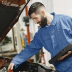 Renault Clio używane: na co uważać przed zakupem? Mechanik w niebieskim kombinezonie sprawdza silnik używanego Renault Clio