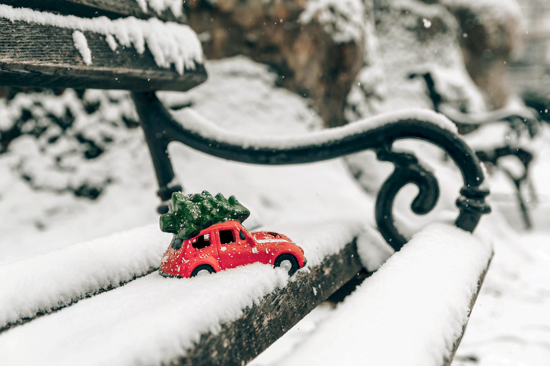 Miniaturowy czerwony Suzuki Ignis z choinką na ośnieżonej ławce