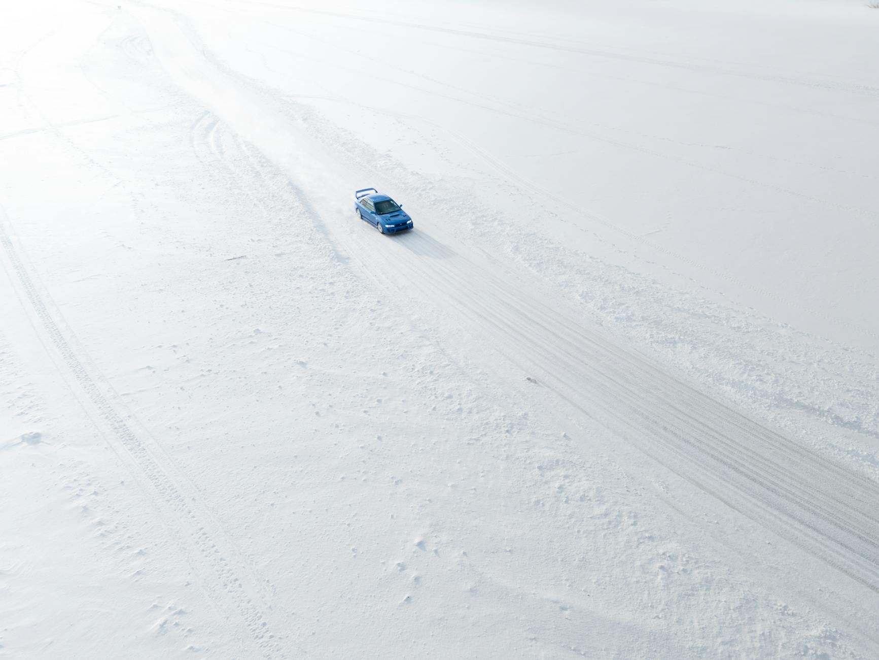 Niebieski Cadillac jadący po zaśnieżonej, otwartej przestrzeni z lotu ptaka