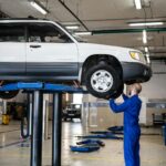 BMW X5 E70: typowe awarie zawieszenia, pneumatyki i napędu na cztery koła Mechanik ogląda białe BMW X5 E70 na podnośniku w warsztacie samochodowym