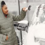 Kobieta w zielonej kurtce odśnieża samochód zimą