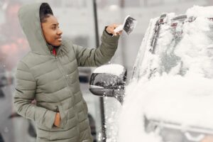 Kobieta w zielonej kurtce odśnieża samochód zimą
