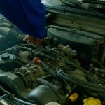Mechanik w niebieskim kombinezonie pracujący przy silniku samochodu w warsztacie